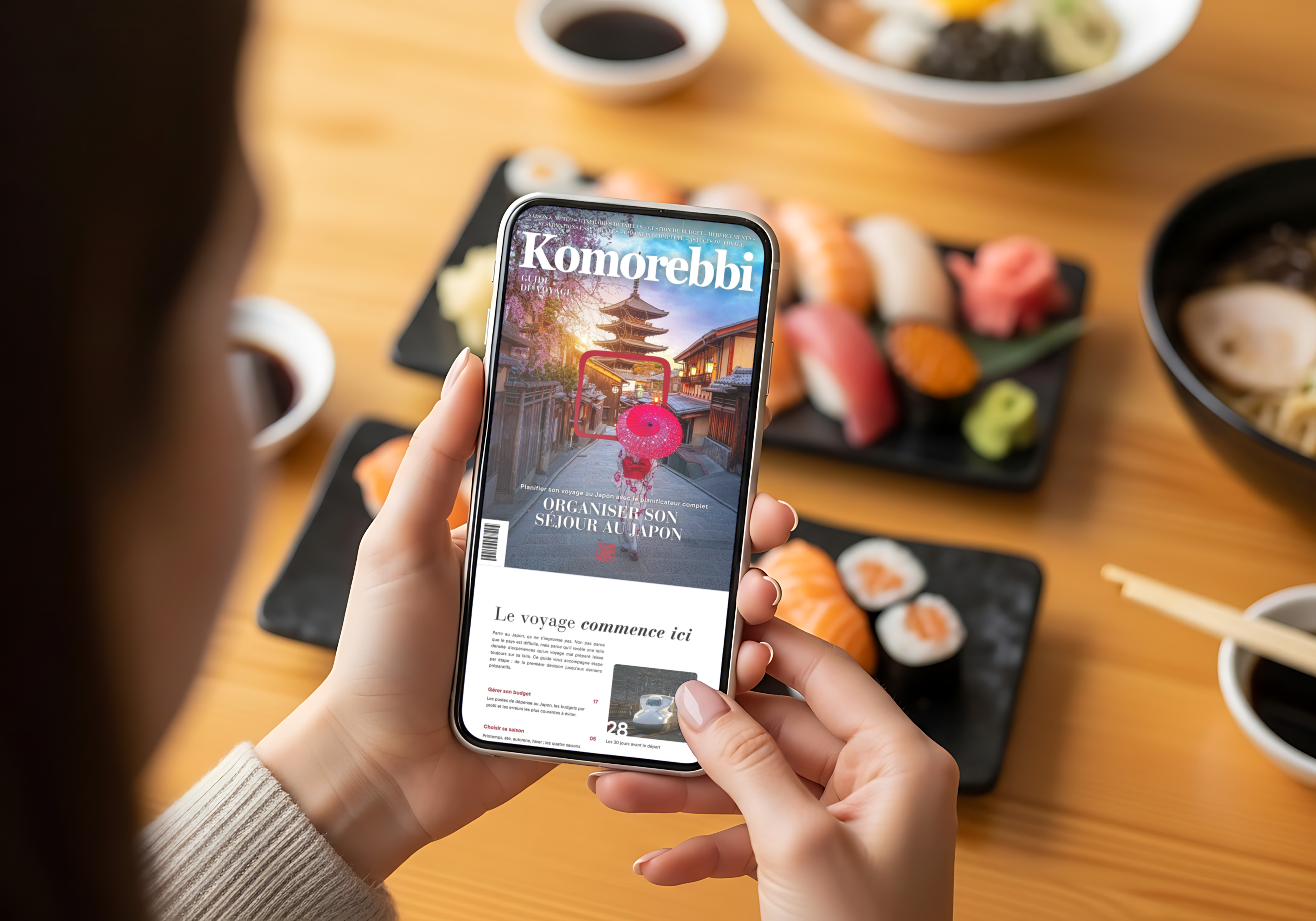 Person holding a smartphone with 'Komorebbi' app open over a table with sushi.